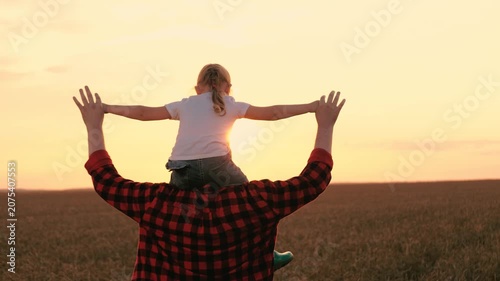 Farmer father walking with daughter on shoulders at sunset dry wheat field back view. Happy family male parent and girl kid child playing flying with open hands at sunrise agriculture meadow closeup
