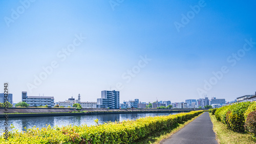 Foto 青空の下に続く川沿いのサイクリングロードと都市風景