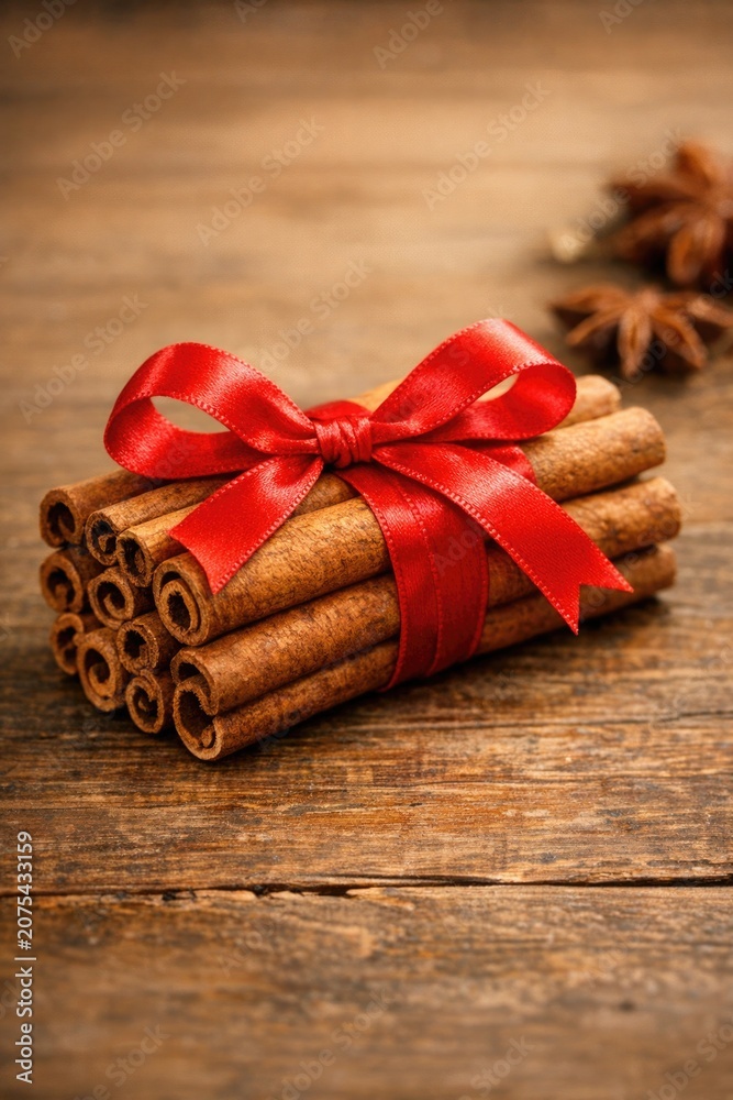 Fototapeta premium A bundle of cinnamon sticks tied with a red ribbon on a rustic wooden table