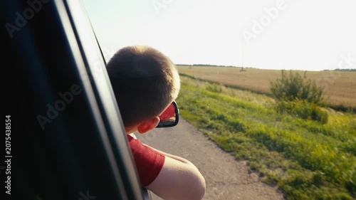 child boy son enjoys summer day with his hand out car window, car rushing along road, child feels wind freedom, car carries child family journey along picturesque road, child car, moving unison with