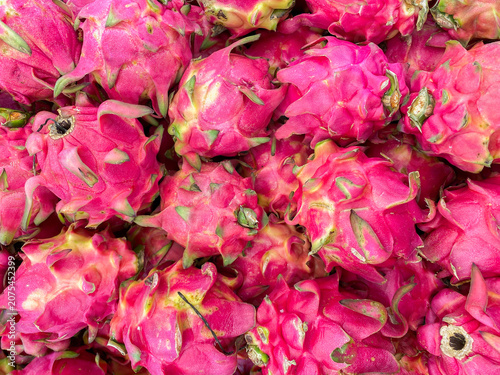 A vibrant and colorful background of fresh dragon fruits or pitaya, showcasing their unique pink skin and green scales in a close-up view.