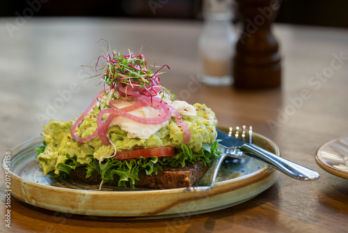 A colorful avocado toast crowned with a silky poached egg, inviting you to slow down and savor the moment. Gourmet avocado toast topped with a perfectly poached egg in a modern café. 