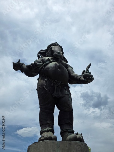 Fotografie Giant Ganesha Statue Under Cloudy Sky: A colossal bronze statue of the Hindu deity Ganesha, with his characteristic elephant head and portly physique