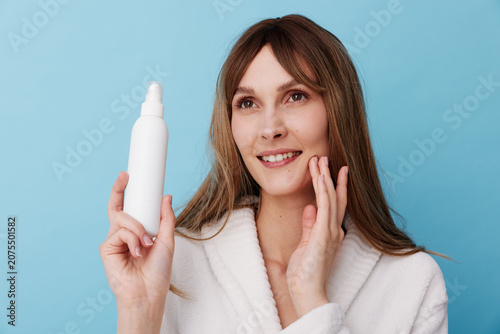 фотографія Cheerful woman in a plush robe holding a spray bottle, preparing a skincare rout