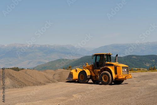 Bild auf Leinwand Heavy industrial road roller compactor vehicle standing on top of a large mound of crushed stone and gravel under a clear blue sky on a bright sunny day