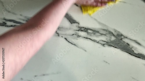 Female hand using a yellow microfiber cloth to wipe and disinfect a white marble kitchen countertop. Routine household chore for home hygiene