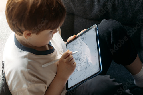 Quadro em tela A child sits on a sofa using a stylus to draw on a tablet