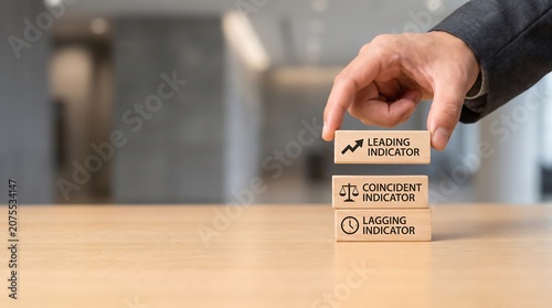 Hand placing wooden block with leading indicator on top of coincident and lagging indicators on desk in office