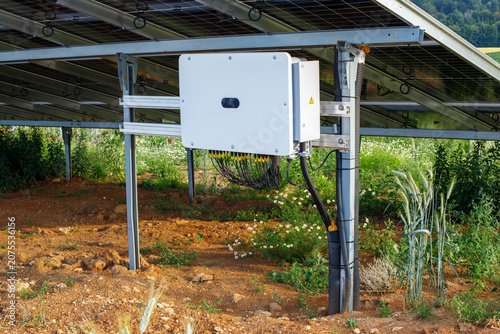 Close-up of a solar inverter box installed under photovoltaic panels on a solar farm infrastructure.