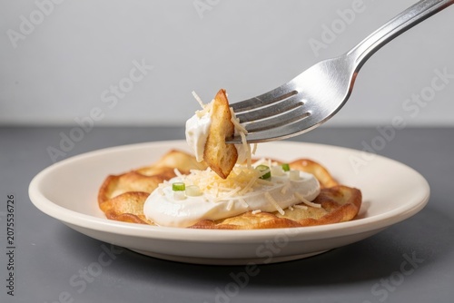 Langos topped with sour cream and grated cheese, sprinkled with green onions on white plate. Concept of fried flatbread with sour cream cheese, focusing on delicious food layout.