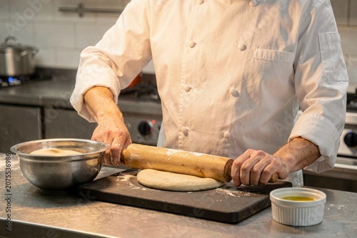 Chef using rolling pin to flatten dough for langos in modern kitchen, atmosphere cozy. Fried flatbread with sour cream cheese showcases culinary skills and fresh ingredients.