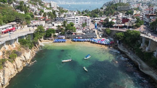 Aerial view of Acapulco's Playa Angosta, a narrow beach teeming with life, colorful umbrellas, boats, and the bustling Mexican coastal city in the background