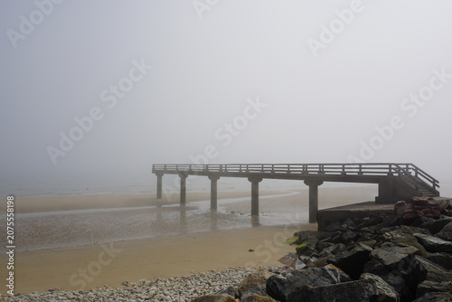 Foto Embarcadero de hormigón en playa con niebla en costa Normandía con marea baja