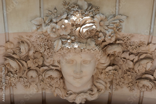Exquisite close-up of a serene female mascaron crowned with an extravagant garland of carved roses and wildflowers on a Champs-Elysees facade in Paris. France.