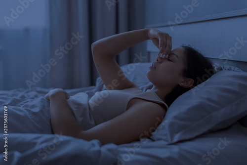 Fotografie Black woman lying awake in bed at night and pinching her nose, suggesting sinus
