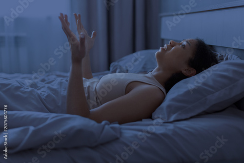 Fotografia Black woman is lying awake in bed at night with raised hands, looking thoughtful