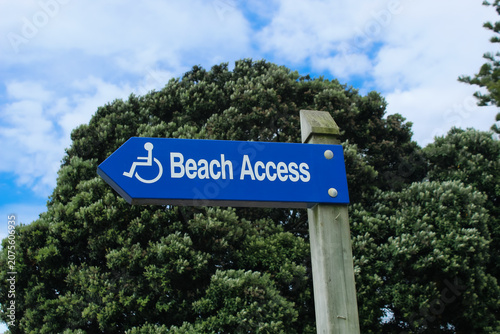 Blue directional sign with wheelchair symbol indicating accessible beach access