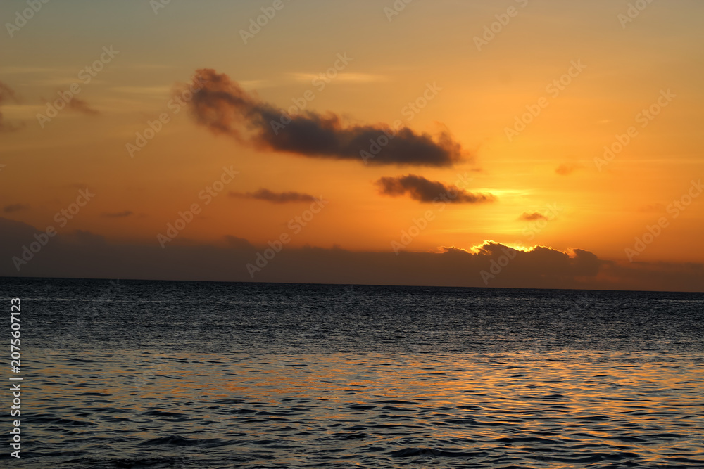 Fototapeta premium Beautiful ocean sunrise with a golden orange sky and dramatic clouds over the calm water surface. seascape background banner.