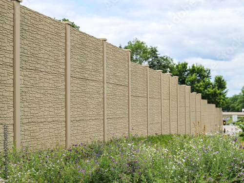 Concrete noise barrier wall with a faux stone texture next to a grassy highway roadside. infrastructure concepts