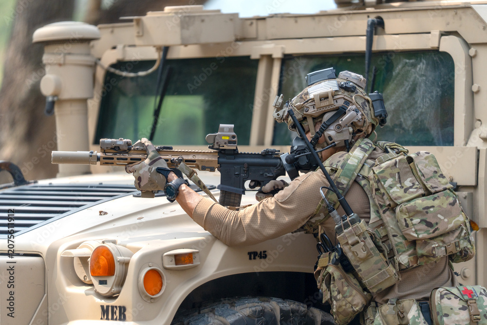 Fototapeta premium One army man point gun to enemy direction and lean on front hood of High Mobility Multipurpose Wheeled Vehicle to practice of fight with enemy.
