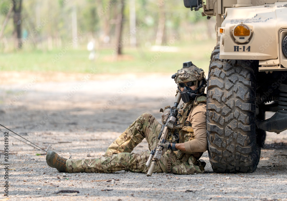 Fototapeta premium One army man sit and lean on right side front wheel of High Mobility Multipurpose Wheeled Vehicle to practice of fight with enemy.