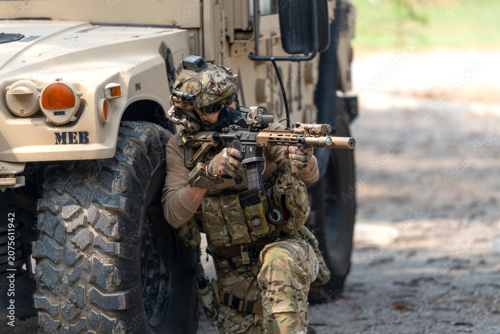 Fototapeta premium One army man sit and lean on left side front wheel of High Mobility Multipurpose Wheeled Vehicle and point the gun to enemy direction.