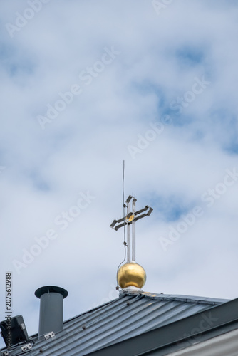 Golden church cross on roof under cloudy sky