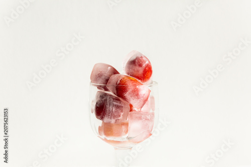 Glaçons avec des cerises rouges givrées à l'intérieur empilés dans un verre sur pied transparent, vue de face en gros plan, arrière-plan blanc