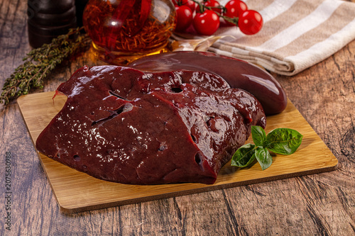 Canvas Print Raw beef liver on wooden cutting board with herbs and tomatoes for cooking