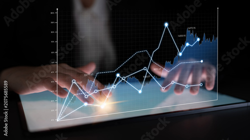 Tablou pe pânză A business professional manipulates digital graphs on a tablet, highlighting data analysis and financial trends in a modern setting