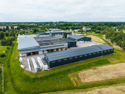 Malpils, Latvia - 24 June 2026: Aerial view of a woodworking manufacturing facility with industrial buildings, storage areas, and green fields in the countryside.