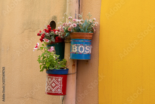 Charming, handmade planters made from recycled tins bearing the city's name, attached to a wall in the colorful streets of Bosa, Sardinia.