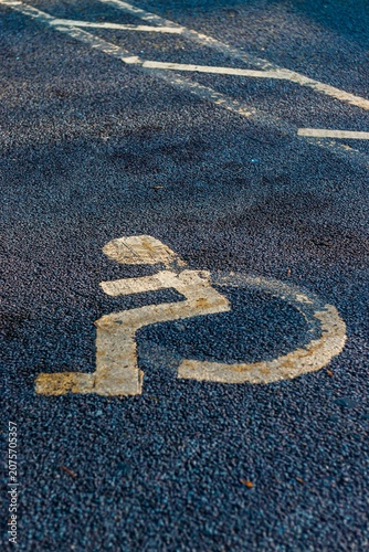 Faded yellow handicap parking icon on wet dark asphalt background perfect for social accessibility advertising corporate inclusion and editorial layouts.