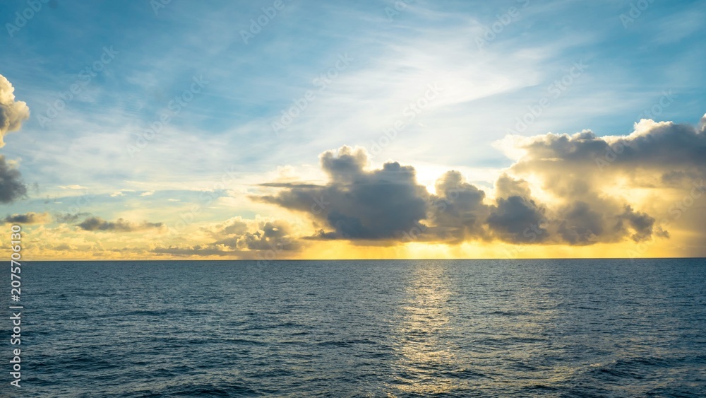 Fototapeta premium Beautiful golden sunrise over calm ocean with dramatic sunbeams breaking through clouds perfect for cruise travel advertising and web banner designs.