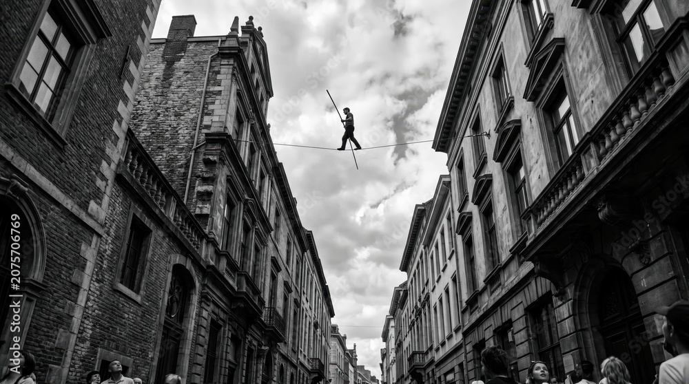 Obraz premium A person balances on a tightrope high above a street filled with people