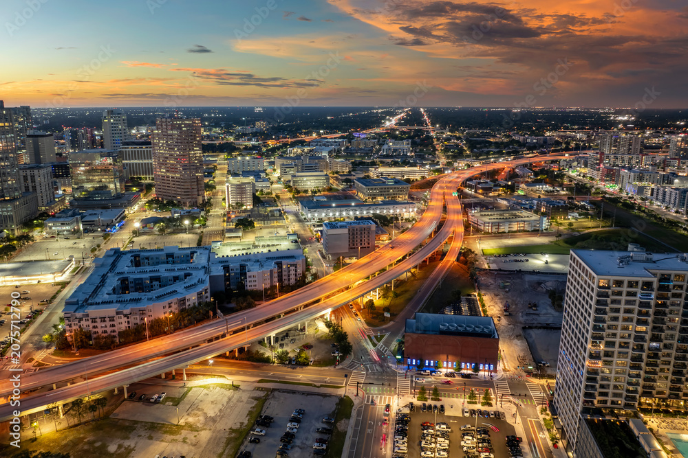 Obraz premium Contemporary nighttime city with elevated highway above downtown streets, moving cars and urban architecture in vibrant American metropolis.