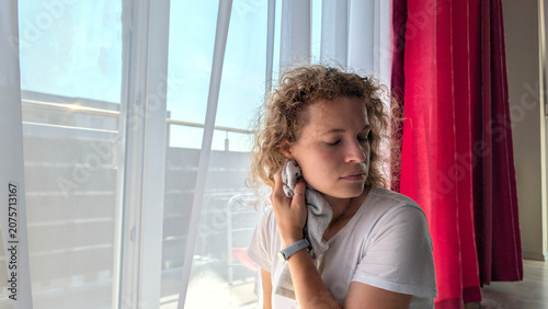 Young Curly Haired Woman Cooling Her Face With Towel By Open Balcony Window
