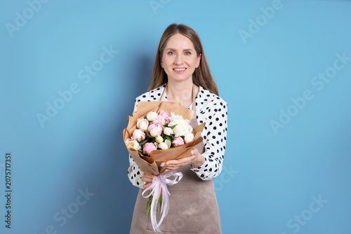 Florist with bouquet of beautiful peonies on light blue background