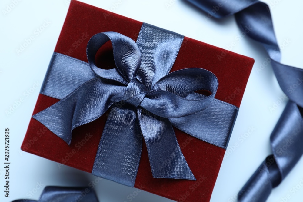 Fototapeta premium Beautiful velvet gift box and ribbon on light blue background, flat lay