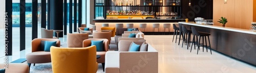 A modern, upscale hotel lounge or bar area. Rows of plush armchairssofas in various colors (mustard yellow, terracotta, beige) with teal pillows. A long bar counter with high stools. A
