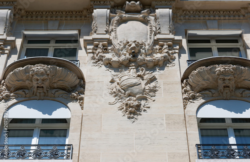 Striking architectural detail on the Champs-Elysees, Paris, featuring two grimacing stone mascarons supporting ornate balconies .