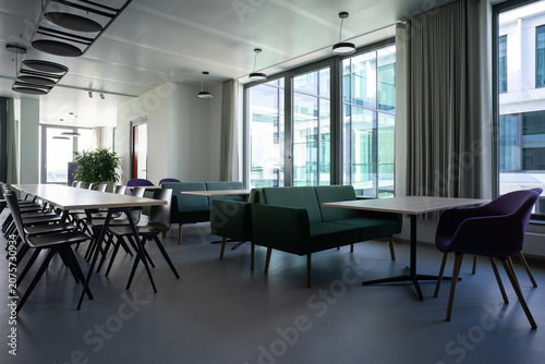 Modern office kitchen and communal workspace with long table chairs lounge area and plants