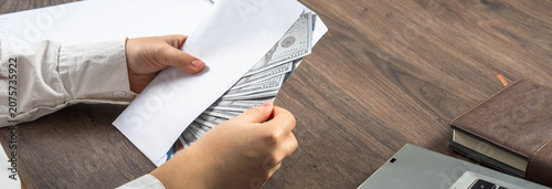 Fotografie Young businesswoman discreetly accepting money, symbolizing corruption, bribery, unethical behavior, and abuse of power in a professional environment, highlighting moral conflict and legal risk