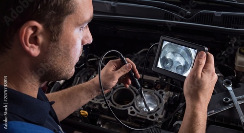 Mechanic using an endoscope camera to inspect the inside of a car engine cylinder for damage.