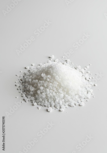 Piles of rough, natural coarse sea salt crystals scattered and heaped upon a clean, bright white surface background for culinary use, grains, spice, pile