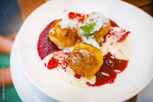 Close-up of traditional Czech sweet dumplings served with strawberries and cream, garnished with powdered sugar and mint, showcasing a delicious dessert in a Prague restaurant