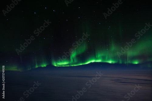 The green Northern Lights Aurora Borealis stretched across the sky above the clouds, as seen from a plane