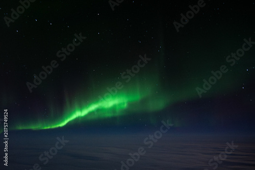 The green Northern Lights Aurora Borealis stretched across the sky above the clouds, as seen from a plane