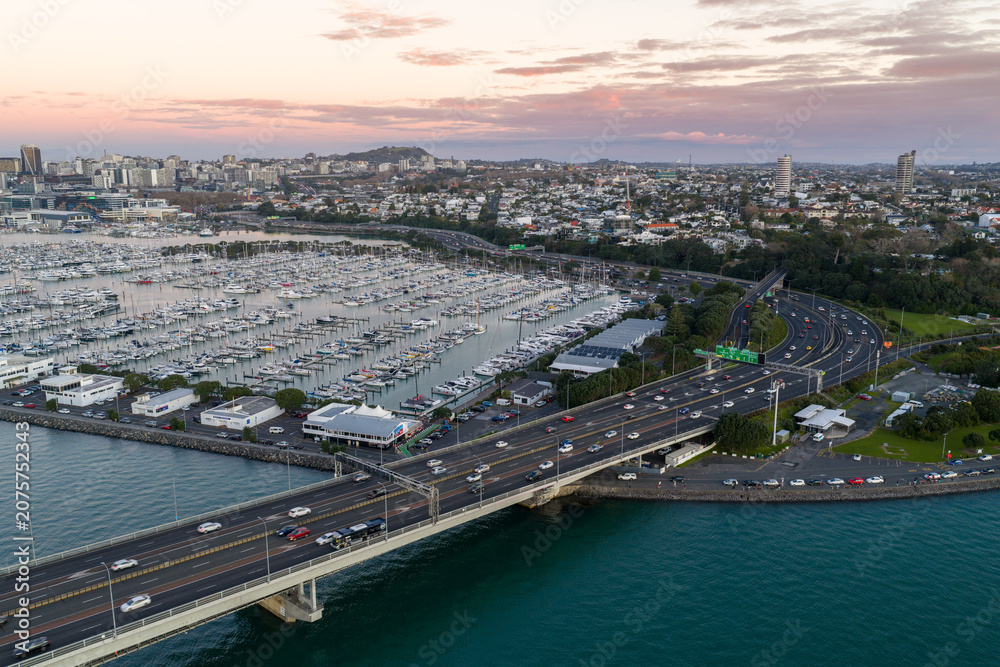 Obraz premium Aerial view of Auckland Harbour Bridge and Viaduct Harbour Marina in Auckland, New Zealand. Cars drive across the bridge during the day.