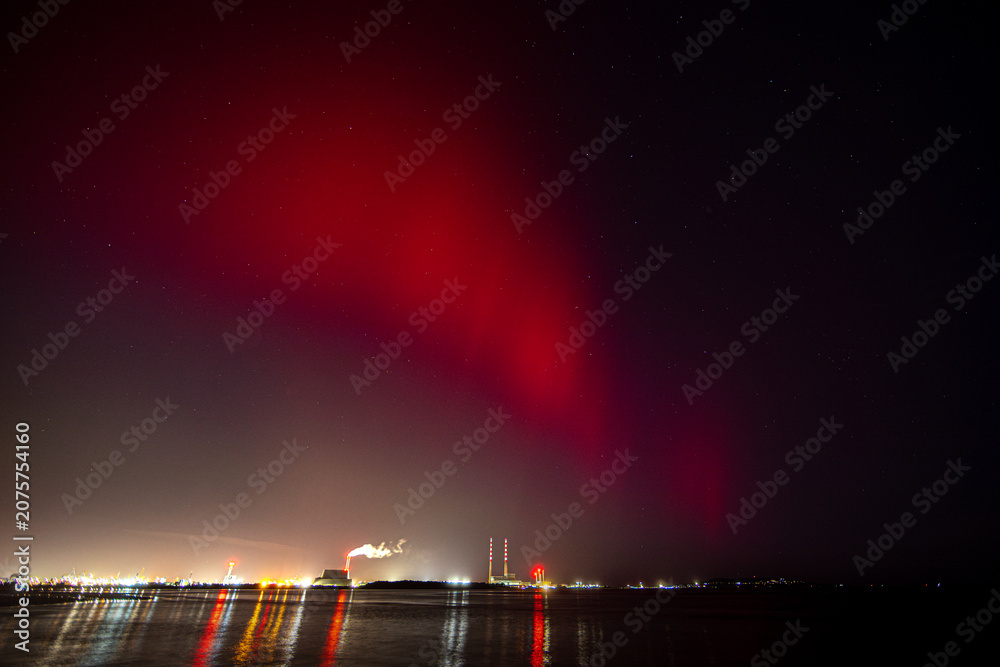 Fototapeta premium The Northern Lights in Dublin, Ireland. Red lights above the Poolbeg Chimneys in Dublin Bay